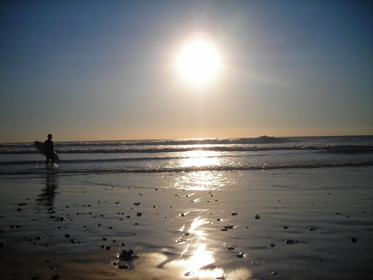 Surfista caminando por la orilla de la playa de El Palmar al atardecer