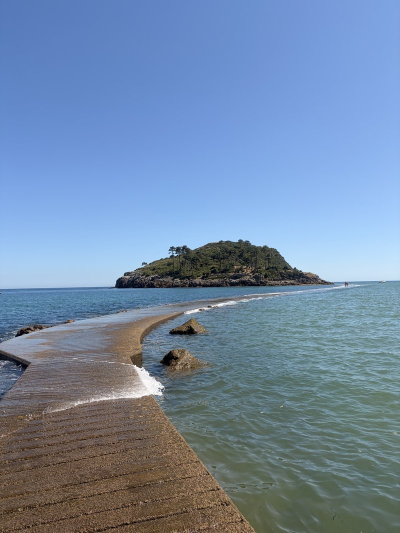Persona caminando por la pasarela hacia la isla de San Nicolás en Lekeitio con olas a ambos lados