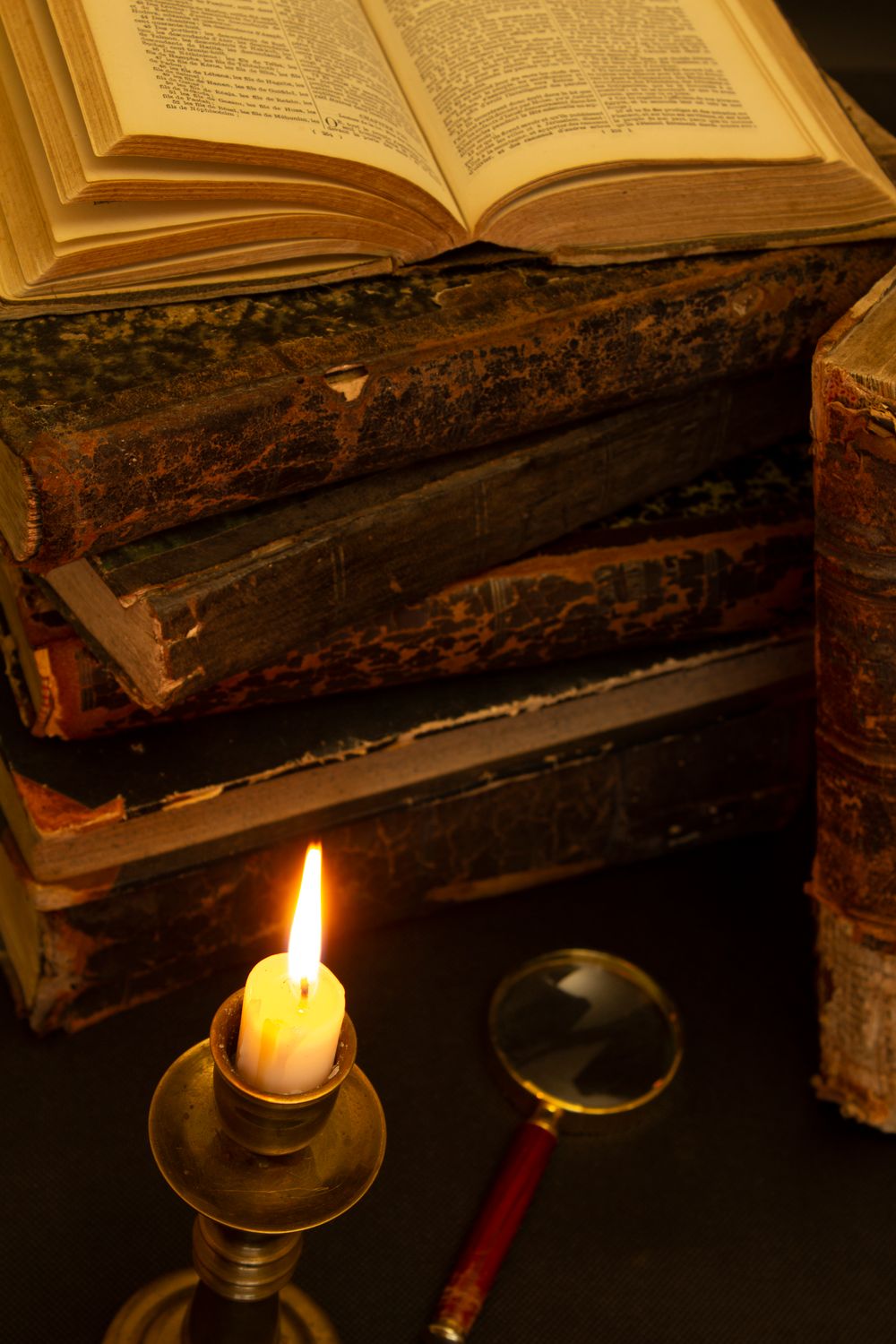 Libros antiguos, una vela y una lupa sobre una mesa, ambiente de misterio de escape room