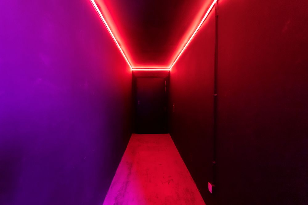 Pasillo oscuro iluminado con luz de neón roja y morada en un escape room de Málaga