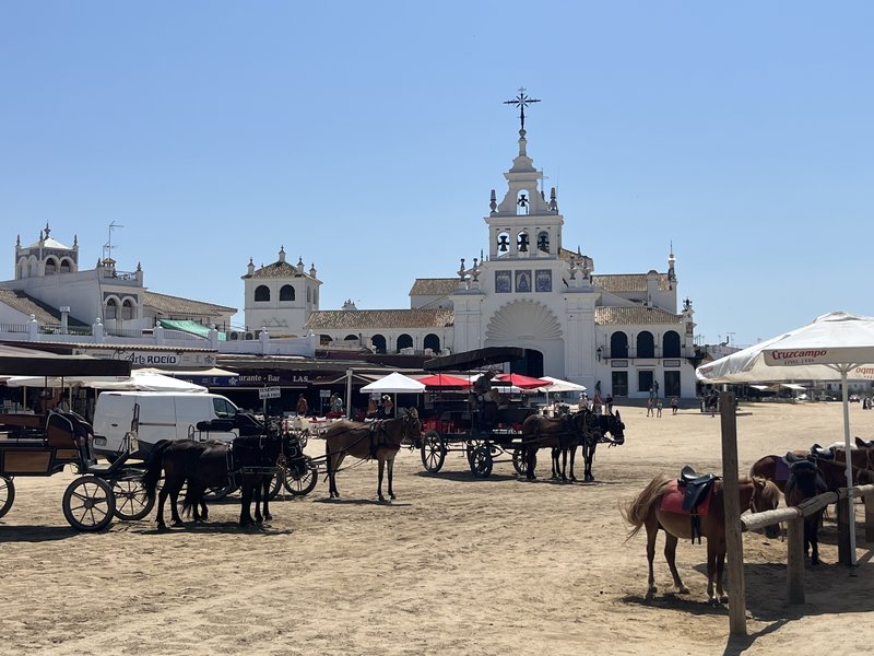 Calle de arena de El Rocío con carruajes de caballos y la ermita al fondo