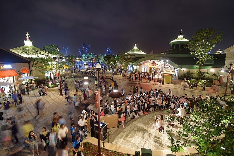 Plaza de Disneytown iluminada de noche con tiendas y restaurantes en Shanghai Disney Resort